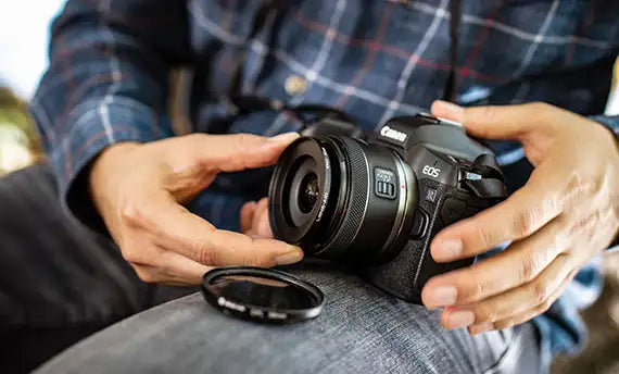 Schwarze Canon EOS M Kamera mit Objektiv und einem abnehmbaren Filterring, der in der Nähe liegt.